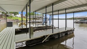 A covered dock with a picnic table and lounge chairs, overlooking a calm body of water.