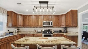 A kitchen with wooden cabinets, a central island with chairs, a built-in microwave, and a hanging light fixture.