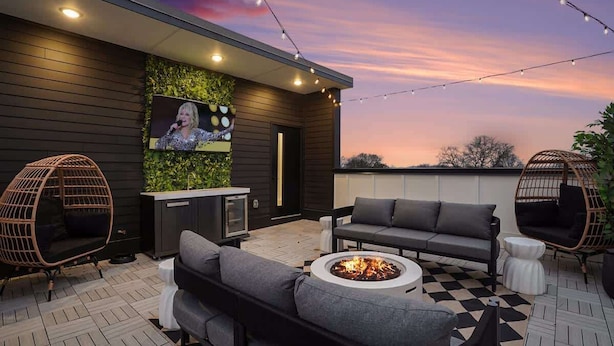 An outdoor patio with a sofa, chairs, a fire pit, and a wall-mounted TV.