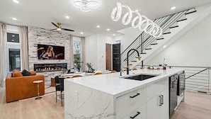 A modern kitchen with a marble island, a built-in TV, and a staircase with a railing.