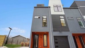 A modern two-story residential building with a garage, a wooden front door, and a small window above the door.
