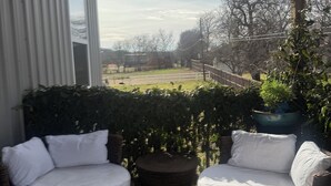 Een overdekt terras met rieten meubilair en uitzicht op een omheinde tuin.