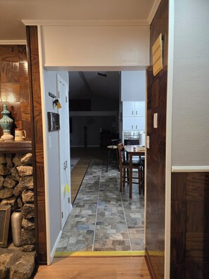 A hallway leading to a dining area with a stone tile floor, wooden cabinets, and a table with chairs.