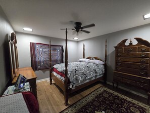 A bedroom with a four-poster bed, a wooden dresser, a ceiling fan, and a patterned rug.