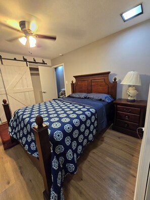 A bedroom with a bed, a nightstand, a lamp, a ceiling fan, and a sliding door closet.