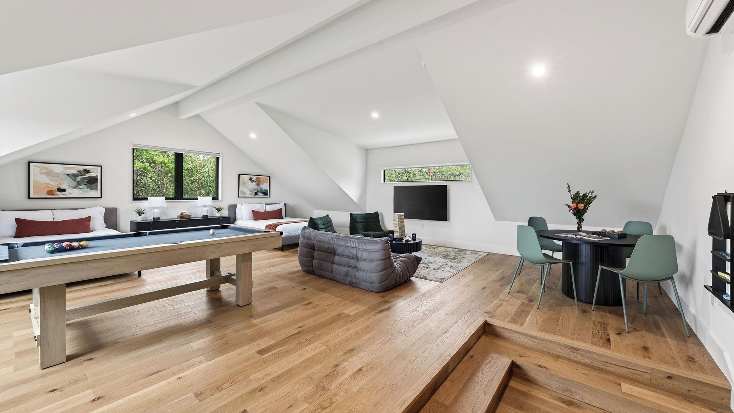 A modern loft with a pool table, seating area, dining space, and large windows.