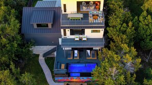 Ein modernes, zweistöckiges Haus mit Dachterrasse, Swimmingpool und großem Fenster mit Blick auf den umliegenden Wald.