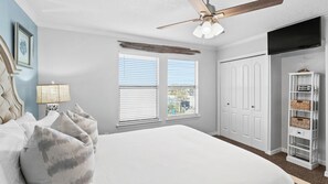 A bedroom with a bed, a ceiling fan, a window with blinds, a wardrobe, and a shelf with baskets. - Beachfront Townhome With Instant Access to Beach Beachside Kisses by Avantstay (Fort Walton Beach)