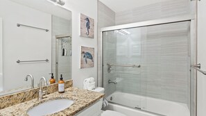 A bathroom with a granite countertop, a sink, a mirror, a glass shower enclosure, and two hand wash bottles. - Beachfront Townhome With Instant Access to Beach Beachside Kisses by Avantstay (Fort Walton Beach)