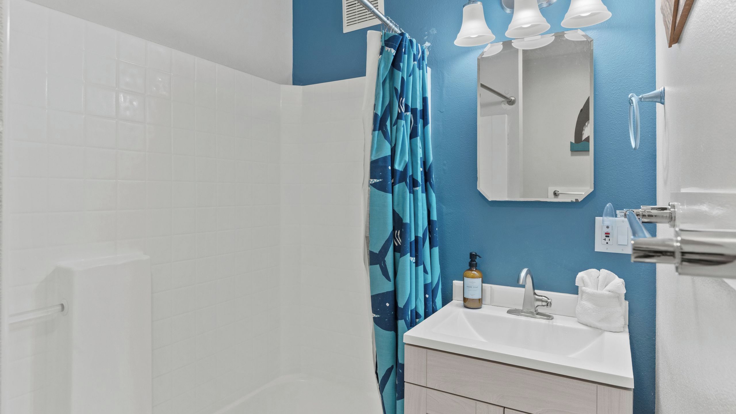 A bathroom with a shower, a sink, a mirror, and a towel rack.