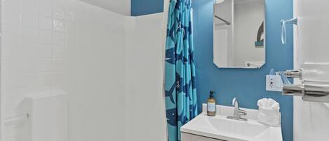 A bathroom with a shower, a sink, a mirror, and a towel rack.