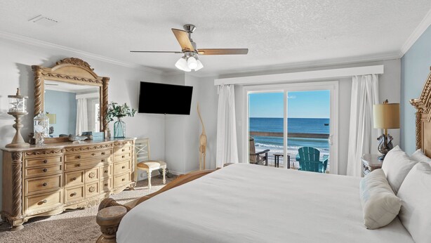 A bedroom with a large bed, a dresser, a television, and a view of the ocean. - Beachfront Townhome With Instant Access to Beach Beachside Kisses by Avantstay (Fort Walton Beach)