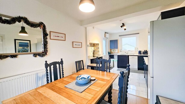 A dining area with a wooden table and chairs, a kitchen with blue cabinets, and a large mirror on the wall. - BrynView - 3 Bedroom Holiday Home - Reynoldston (Swansea)