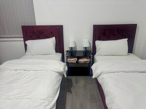 A hotel room with two beds, white bedding, a dark red headboard, and a nightstand with two lamps and towels.