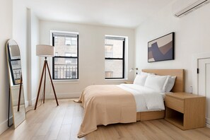 A modern bedroom with a bed, bedside table, lamp, and a large window. - Blueground | Midtown East, washer/dryer, nr UN (New York)
