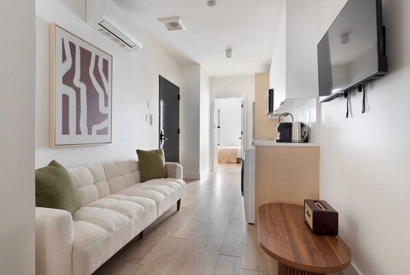 A modern, minimalist living space with a sofa, a coffee table, and a flat-screen TV mounted on the wall. - Blueground | Midtown East, washer/dryer, nr UN (New York)