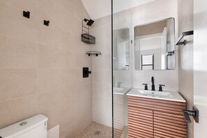 A modern bathroom with a glass shower enclosure, a white toilet, and a vanity with a mirror and sink. - Blueground | Midtown East, washer/dryer, nr UN (New York)