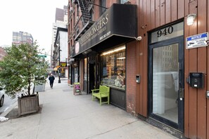 A storefront with a sign reading "CHEESEMONGERS" and a phone number. There is a green bench outside, and a "NOTICE" sign about 24-hour video surveillance. - Blueground | Midtown East, washer/dryer, nr UN (New York)