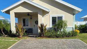 Einbungalow mit überdachter Veranda, Eingangstür und kleinem Vorgarten mit Pflanzen sowie einem gepflasterten Einfahrtsweg.