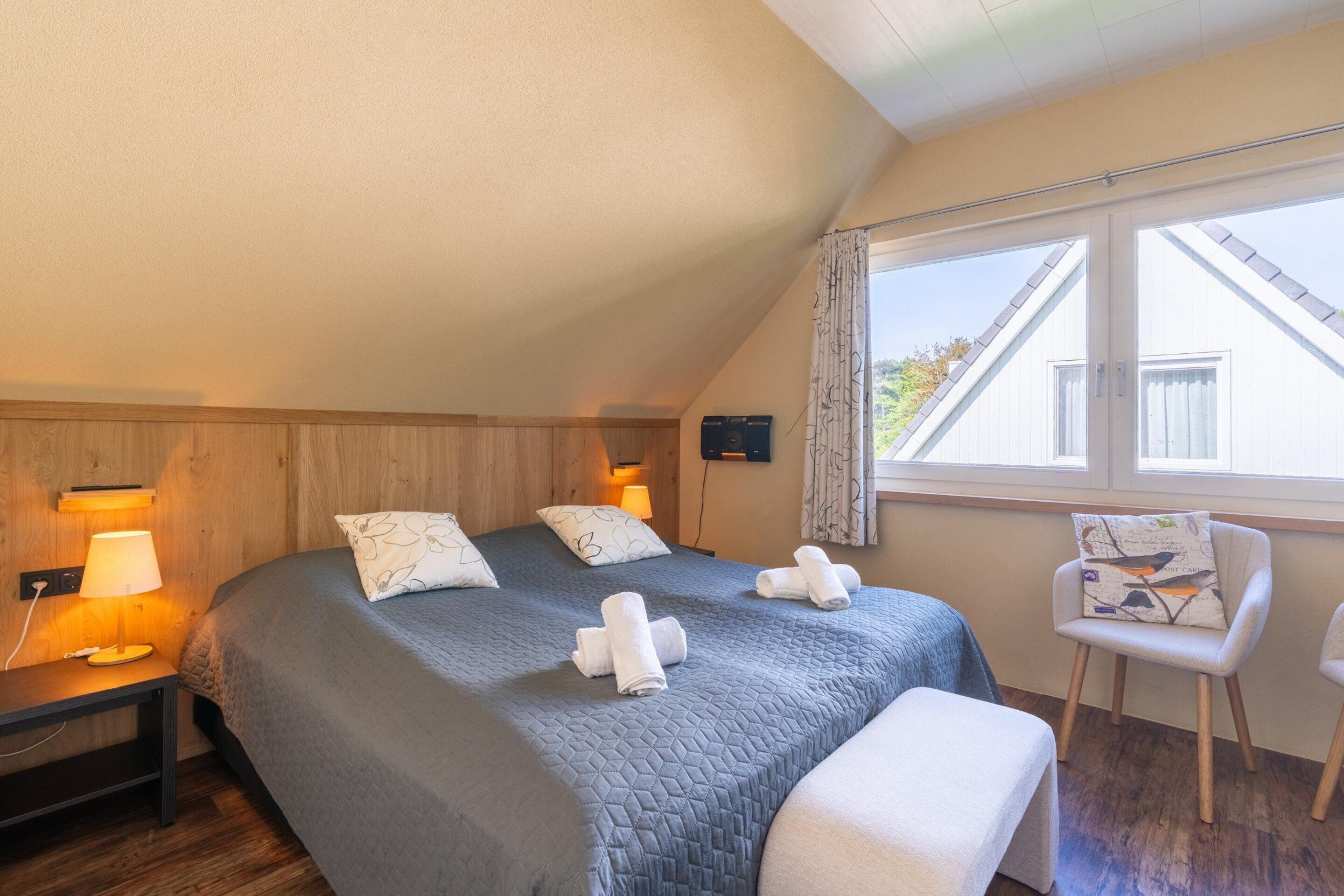 A bedroom with a bed, bedside lamps, a chair, and a window.