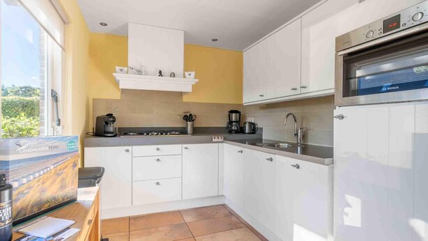 A compact kitchen with white cabinets, a built-in oven, and a coffee maker. - Very Tastefully Furnished Country House for 4 People (Den Burg)