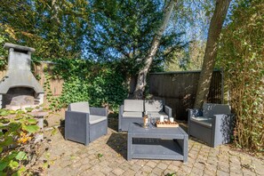 Eine Terrasse im Freien mit Korbmöbeln, einem Steinkamin und einem Holztisch, der mit Kerzen und Snacks gedeckt ist.
