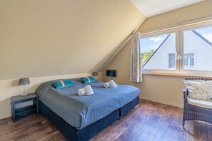 Ein Schlafzimmer mit einem Bett, einem Nachttisch, einer Lampe, einem Fenster mit Vorhängen und Blick ins Freie.