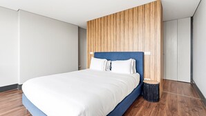 A modern hotel room with a large bed, wooden panel wall, and a small side table. - GuestReady - Ideal Porto stay near Trindade 4th (Porto)
