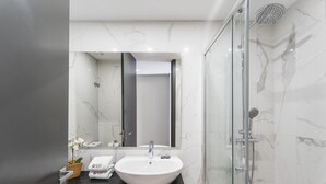 A modern bathroom with a large mirror, a white sink, and a glass-enclosed shower. - GuestReady - Ideal Porto stay near Trindade 4th (Porto)