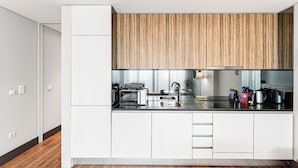 A modern kitchen with white cabinetry, a wooden accent wall, and stainless steel appliances. - GuestReady - Ideal Porto stay near Trindade GF-B (Porto)