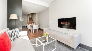 A modern living room with a sofa, a coffee table, a TV, and a dining area with a staircase in the background. - GuestReady - Ideal Porto stay near Trindade GF-F (Porto)