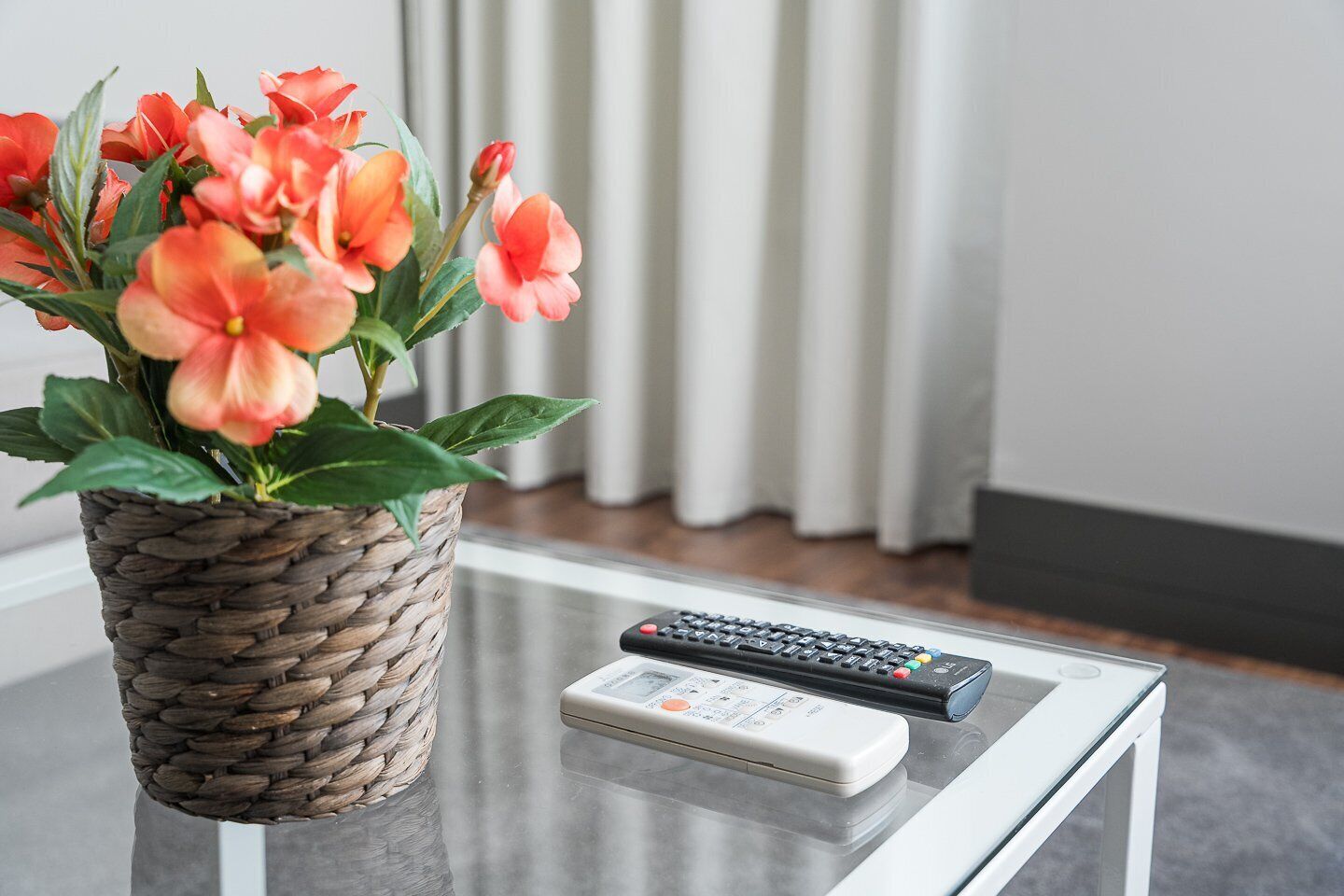 A remote control and a woven basket with flowers on a glass table.