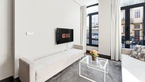 A modern hotel room with a flat-screen TV, a sofa, a glass coffee table, and large windows offering a city view. - GuestReady - Ideal Porto stay near Trindade GF-F (Porto)