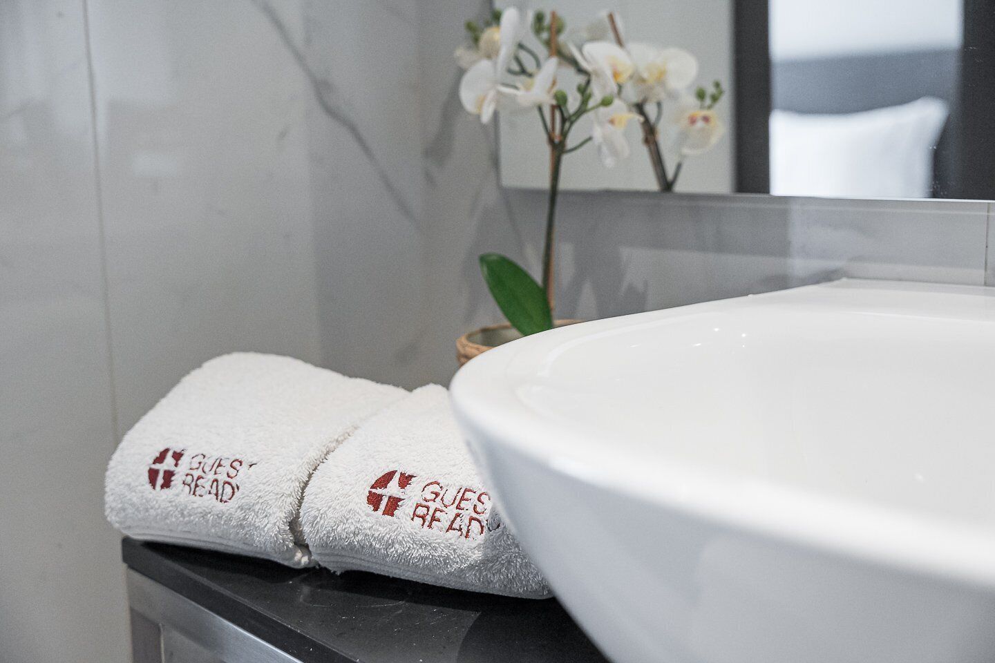 A bathroom with a white sink, a towel with 'Goes Ready' text, and a vase with white flowers.