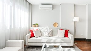 A modern living room with a white sofa, red and white cushions, a coffee table, and a floor lamp. - GuestReady - Ideal Porto stay near Trindade 2nd (Porto)