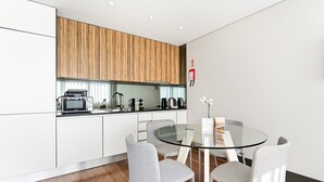 A modern kitchen with white cabinets, a wooden upper section, and a glass dining table with four grey chairs. - GuestReady - Ideal Porto stay near Trindade 2nd (Porto)