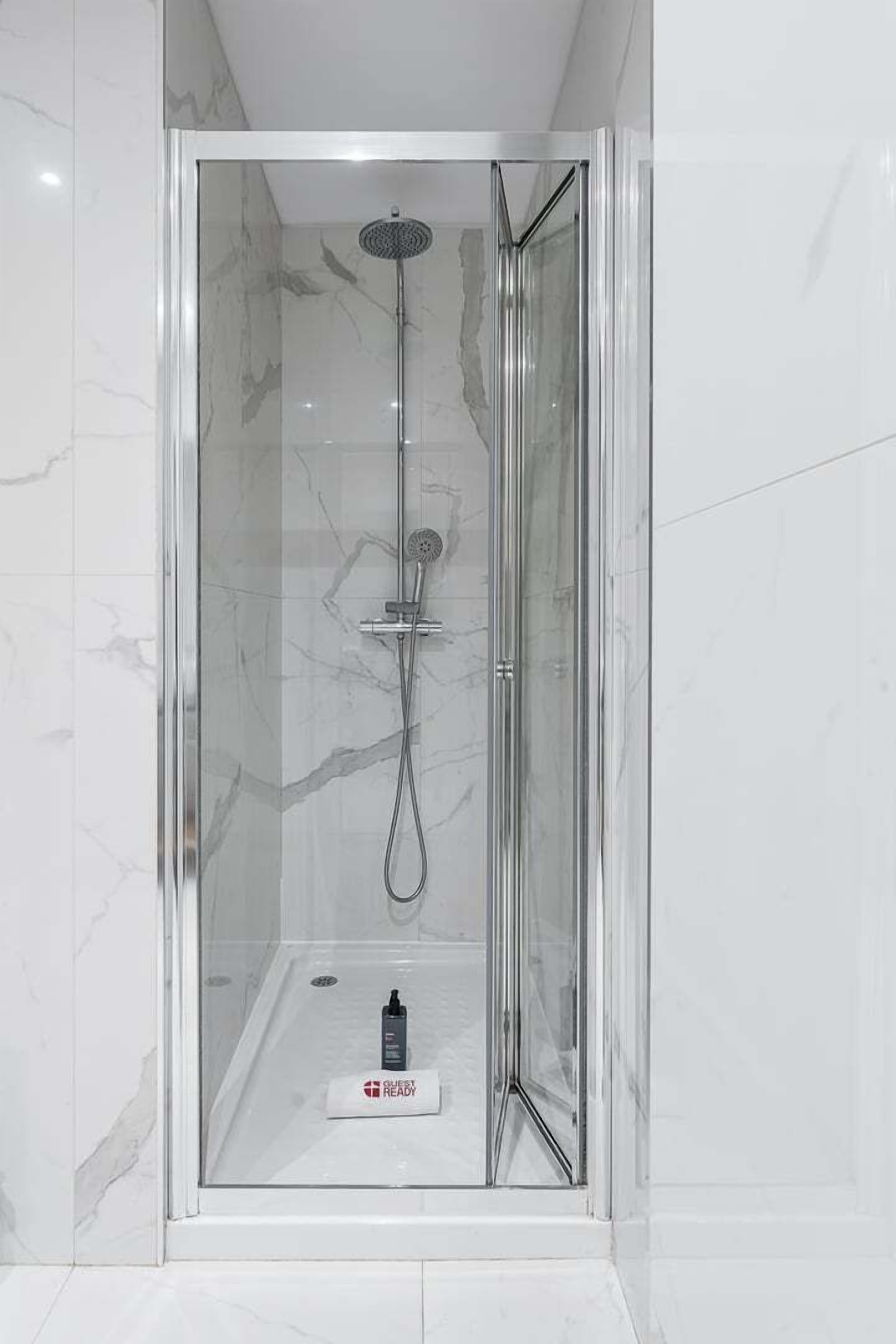 A glass-enclosed shower with a handheld showerhead and a wall-mounted faucet.