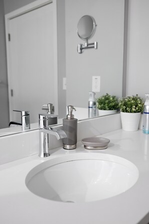 Ein Badezimmer mit einem weißen Waschbecken, zwei Wasserhähnen, einem Spiegel und einer Topfpflanze.