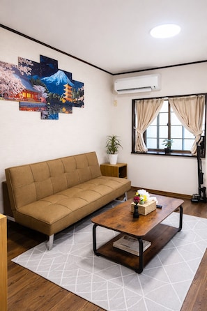 A living room with a sofa, a coffee table, a potted plant, and a window with curtains. - Maison du Skytree (Tokyo)