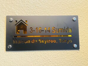 Une plaque métallique représentant un pictogramme de maison et indiquant l’adresse suivante : « 3-16-14 Sumida, Maison du Skyreee, Tokyo ».