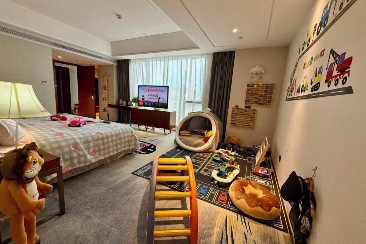 Habitación de hotel con cama, televisión, zona de juegos y pared con dibujos infantiles.