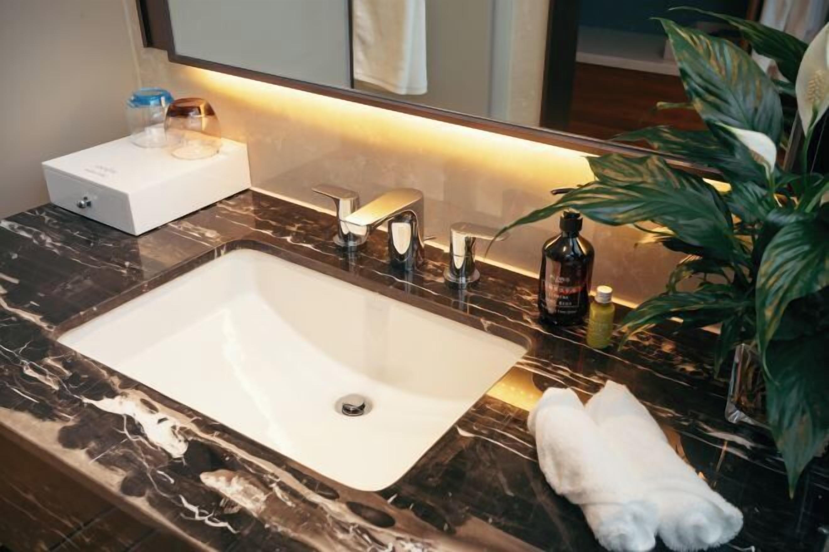 A bathroom with a marble sink, a mirror, a towel, and a plant.