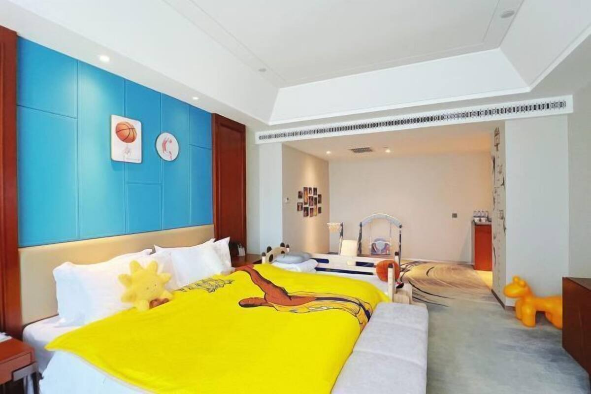 Habitación de hotel con una cama grande, un cabecero azul y un baño pequeño visible a través de una puerta abierta.