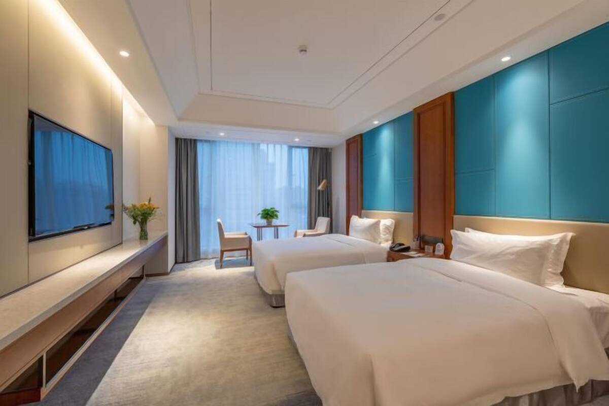 Habitación de hotel con dos camas, televisión, escritorio con silla y vista al exterior.