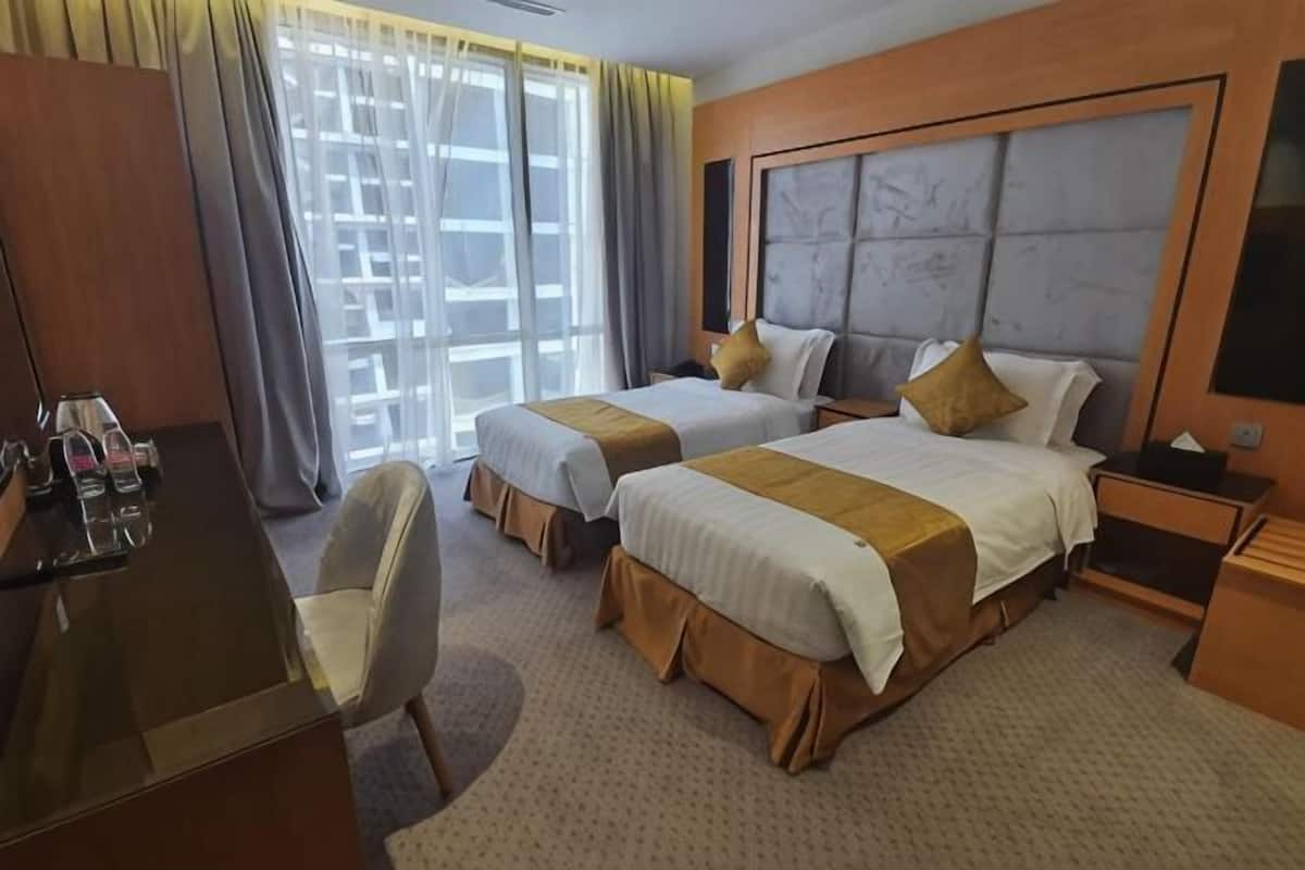 Habitación de hotel con dos camas, un escritorio, una silla y un ventanal con cortinas.