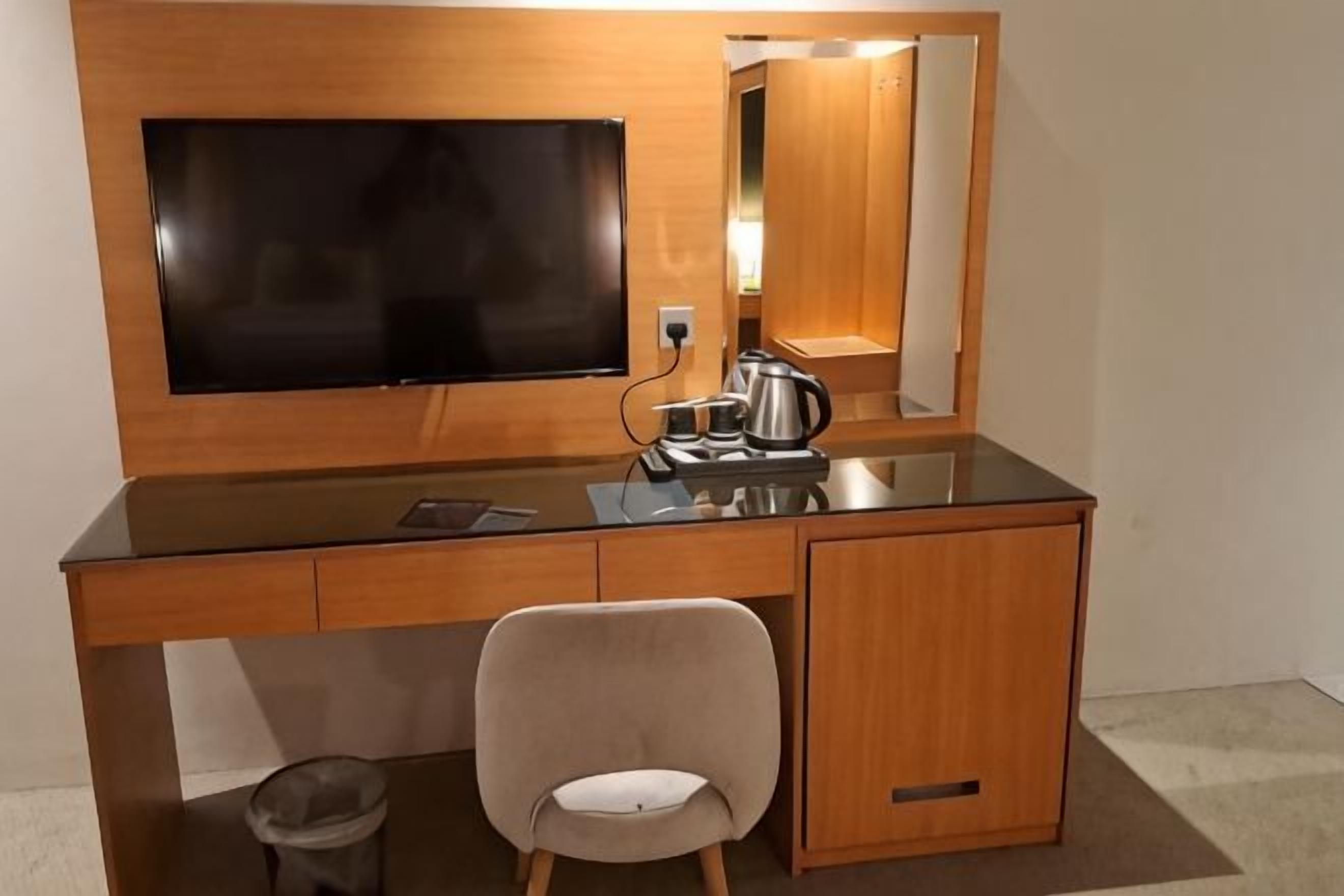 A hotel room with a wooden desk, a chair, a flat-screen TV, a mirror, and a coffee maker.