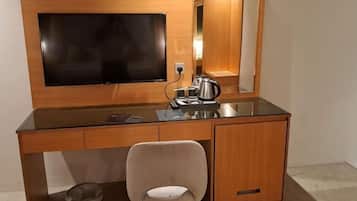 A hotel room with a wooden desk, a chair, a flat-screen TV, a mirror, and a coffee maker.
