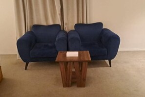 A blue sofa and a small wooden table in a room with beige curtains. - Al Rayyan Tower (Jeddah)
