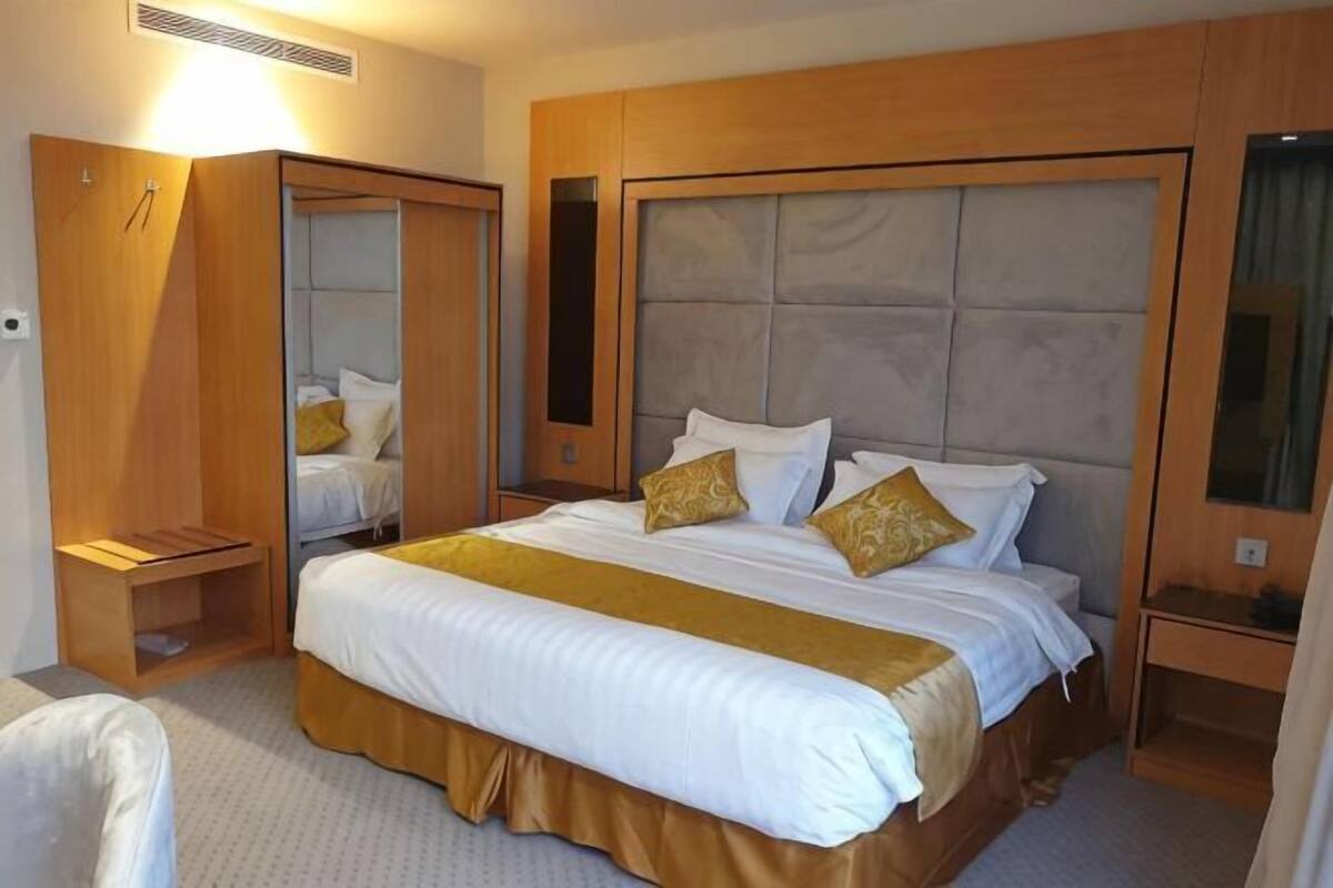 Una habitación de hotel con una cama grande, un armario, una mesita de noche y un espejo.
