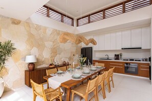 Eine moderne Küche mit weißen Schränken, einem eingebauten Backofen und einem Essbereich mit Steinwand und Korbstühlen.